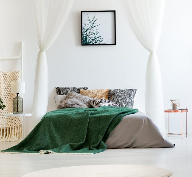 Copper nightstand and ladder blanket rack next to big bed with green quilt in white bedroom of spacious apartment