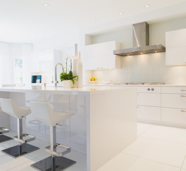 Modern kitchen with white Italian lacquered kitchen island and chrome barstools inside luxury residential home